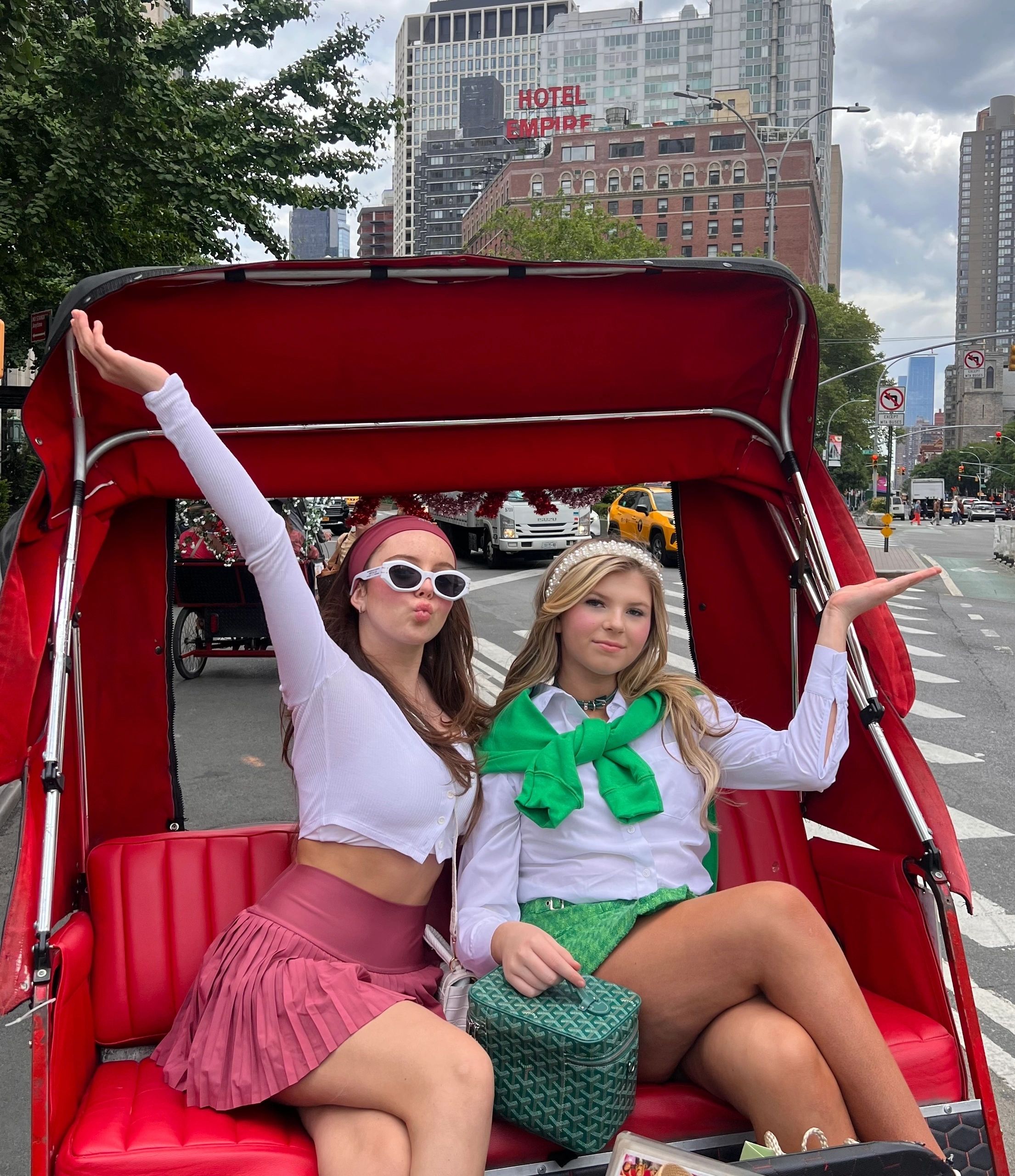 Two guests waving from a red pedicab beside the Hotel Empire on a Gossip Girl tour in NYC