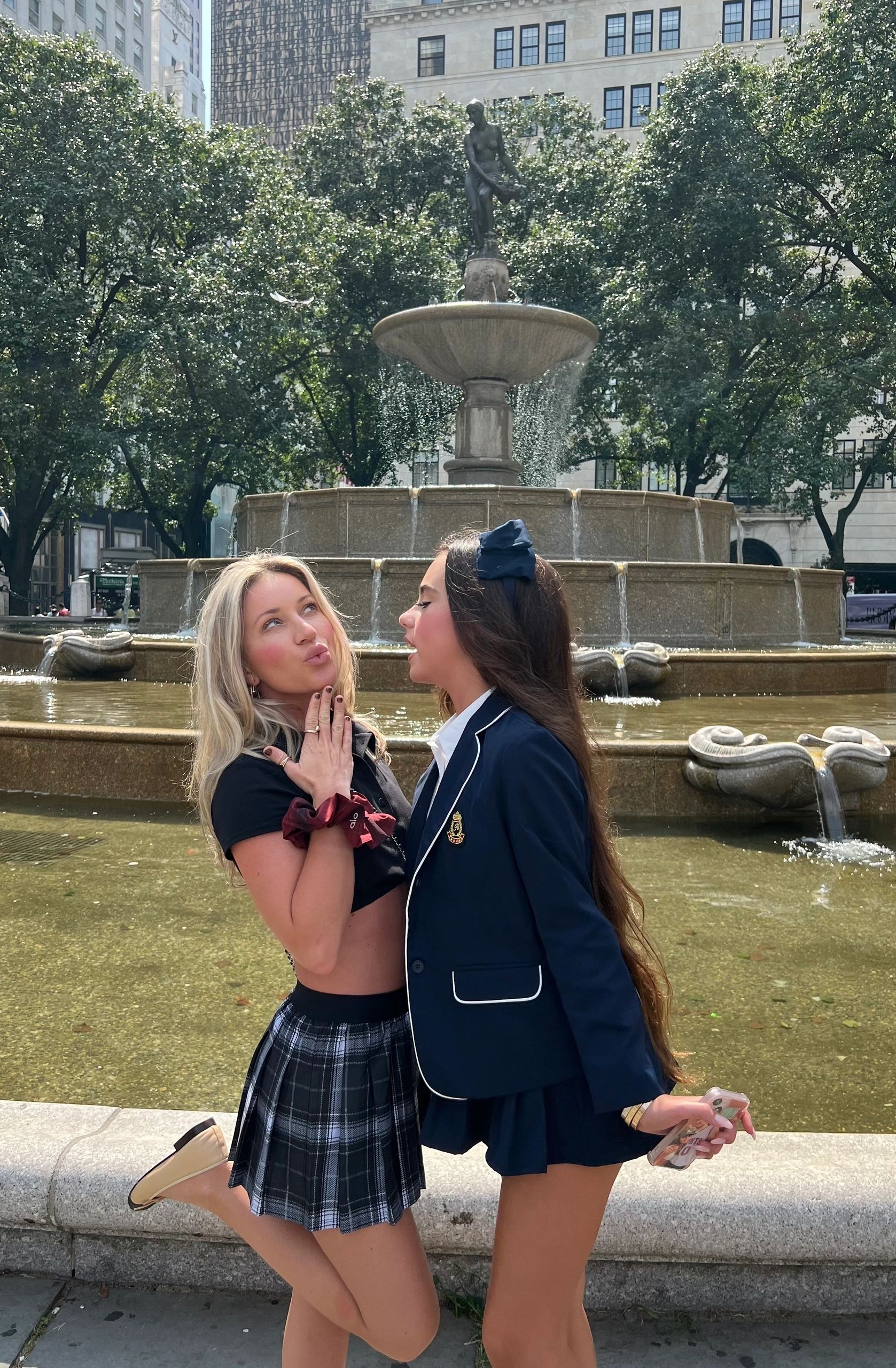 Guest in a plaid schoolgirl skirt posing at the Pulitzer Fountain on a Gossip Girl tour